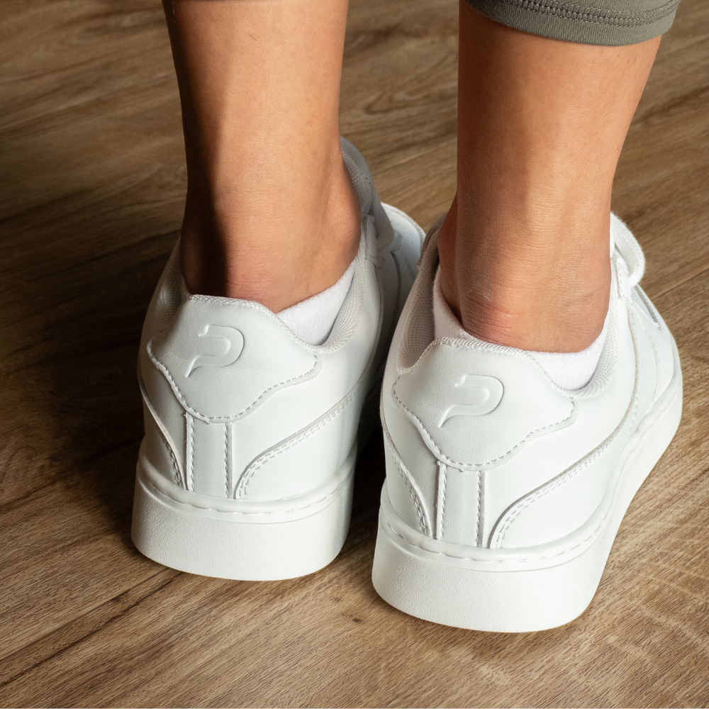 Back view of white low-top Pulse Dance Shoes dance sneakers on a wooden floor, with white ankle socks and heel logos