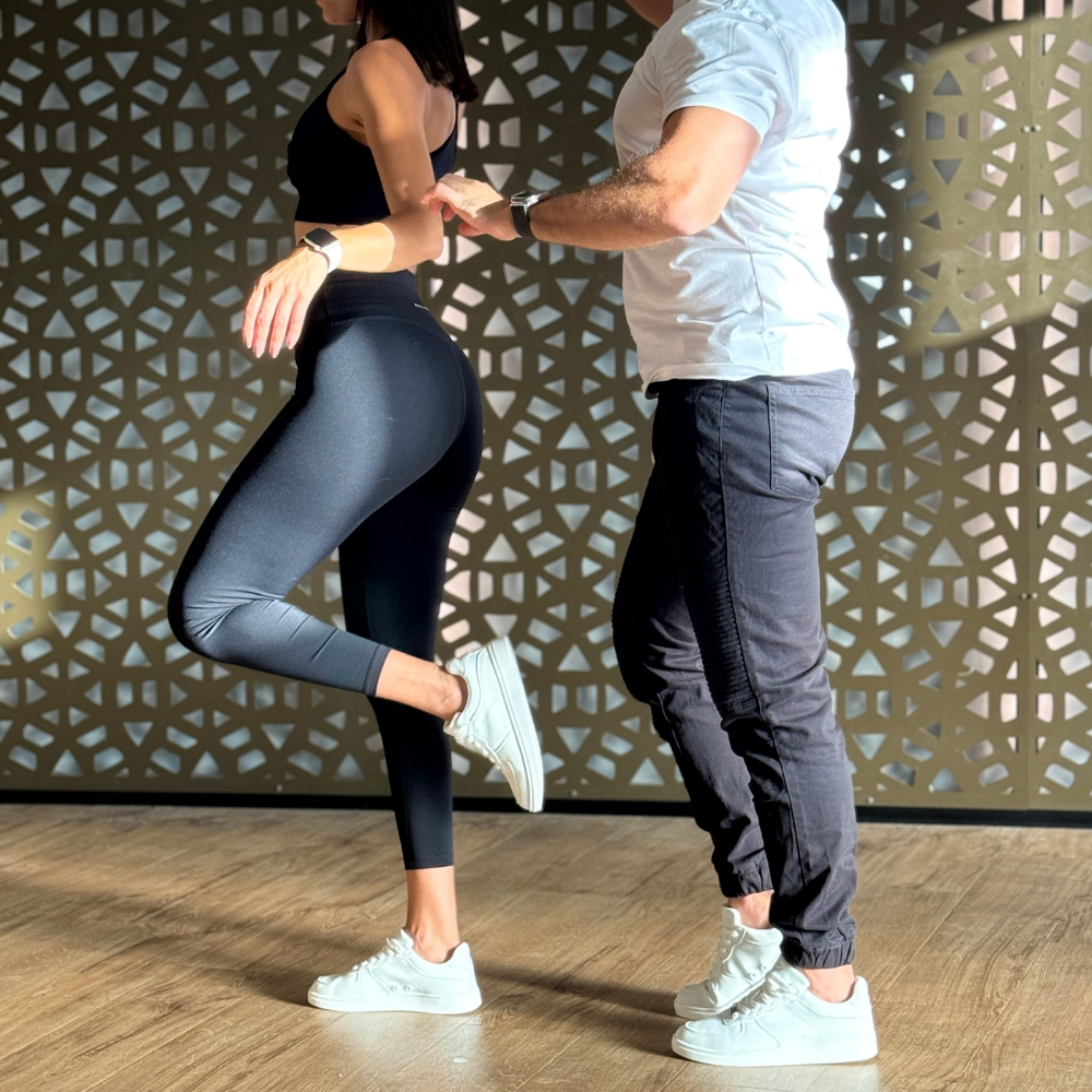Couple practicing partner dance in a studio by a gold lattice wall, both in white Pulse Dance Shoes dance sneakers