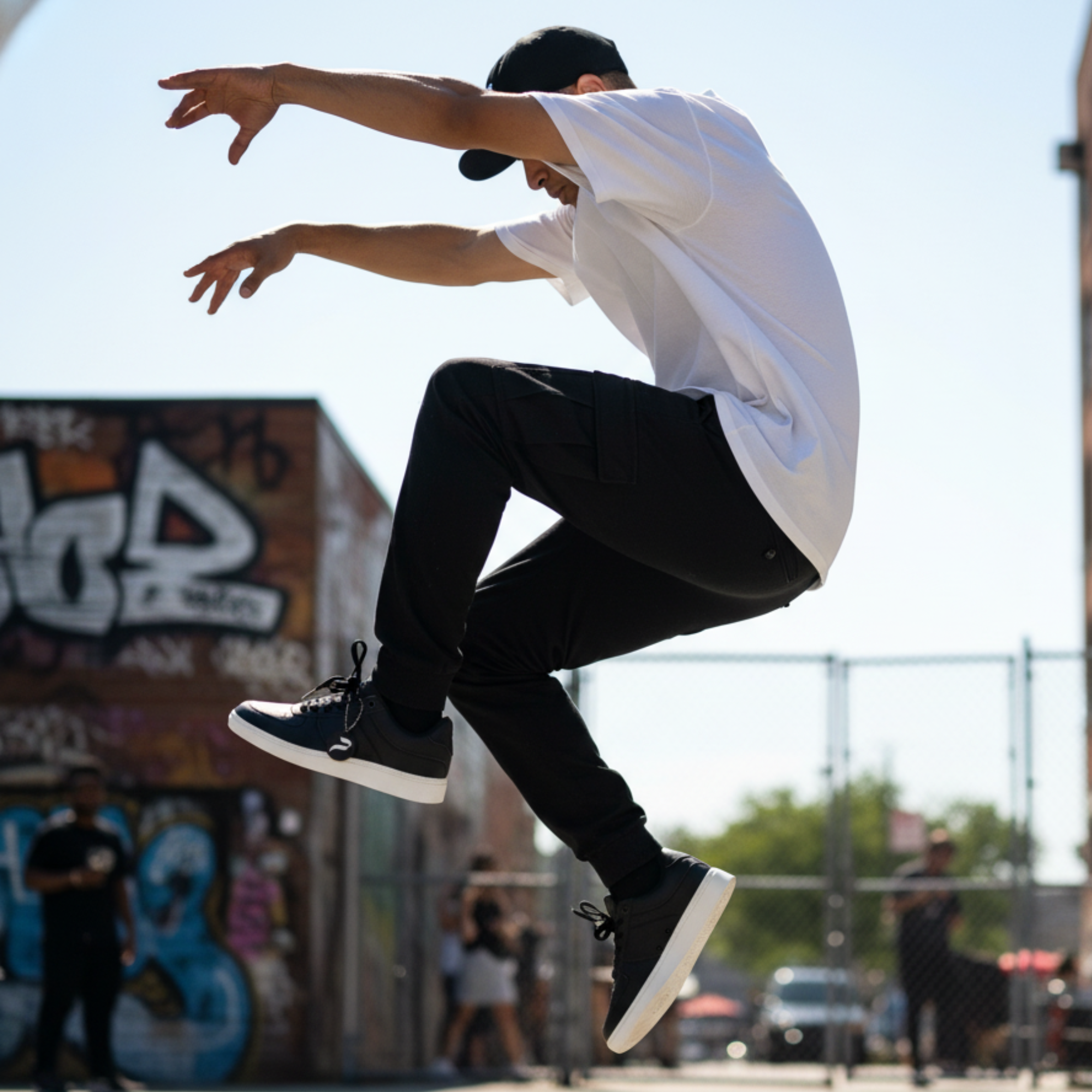 HIPHOP Dancer in white shirt and black pants jumping in an urban setting with graffiti wearing black and white dance sneakers