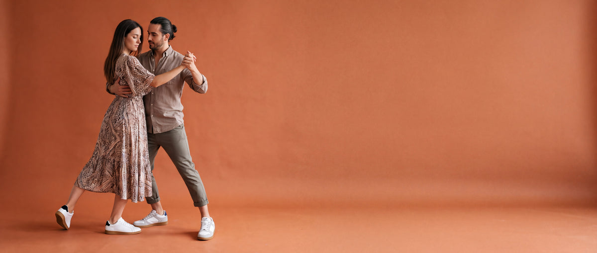 A couple dancing in dance sneakers against a terracotta studio wall
