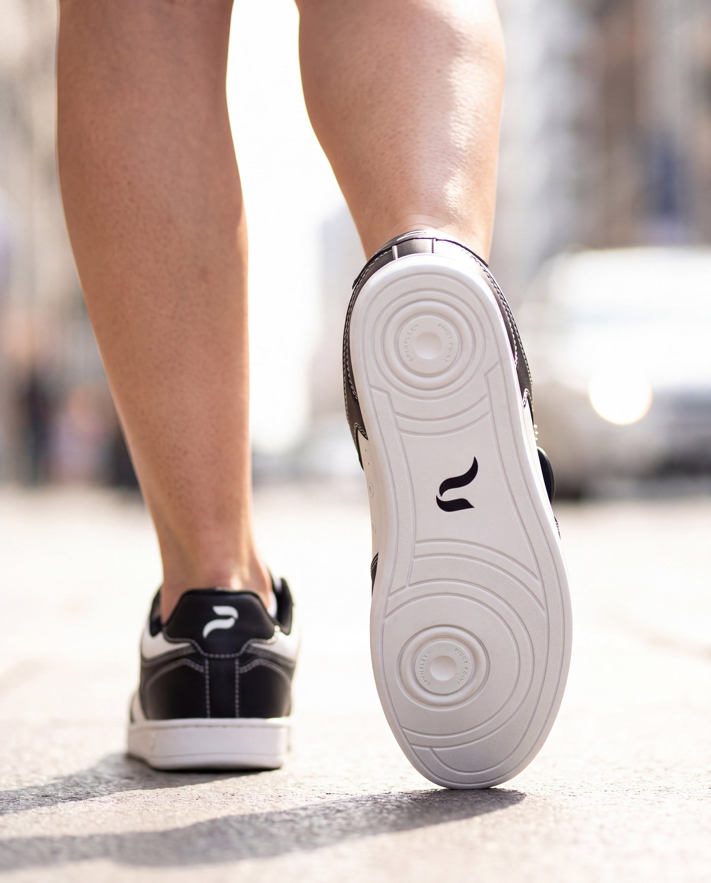 Close-up of a Flow 2 Static dance sneaker mid-stride on a city street, with the SPYNFLEX® pivot point sole facing the camera